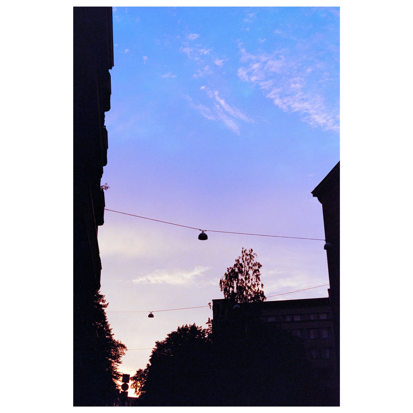 A large gradient sky, from a white to a purple and blue. The dark outline of city buildings an street lights is visible on the sides and bottom.