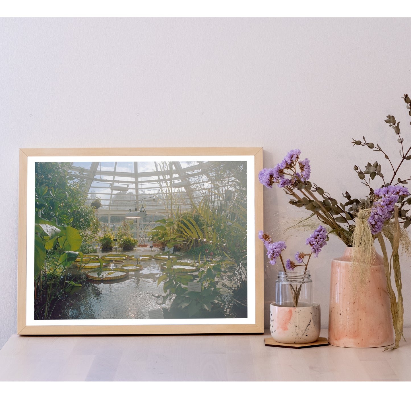 Detail of the 30x40 size photo in a frame, next to a ceramic pot with flowers. It is larger than the pot, and equal height to most of the flowers. In width, it is larger than two to three of the pots next to each other.